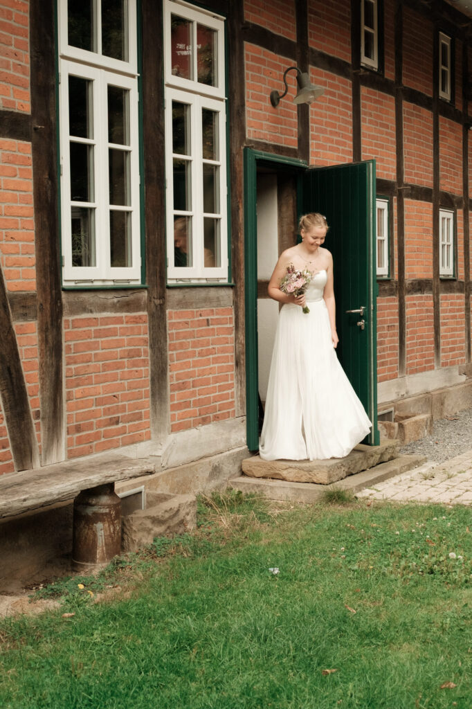 Braut tritt aus der Tür des Fachwerkhauses, Hochzeit Anne & Phil auf dem Hof Gottschalk in Helpsen